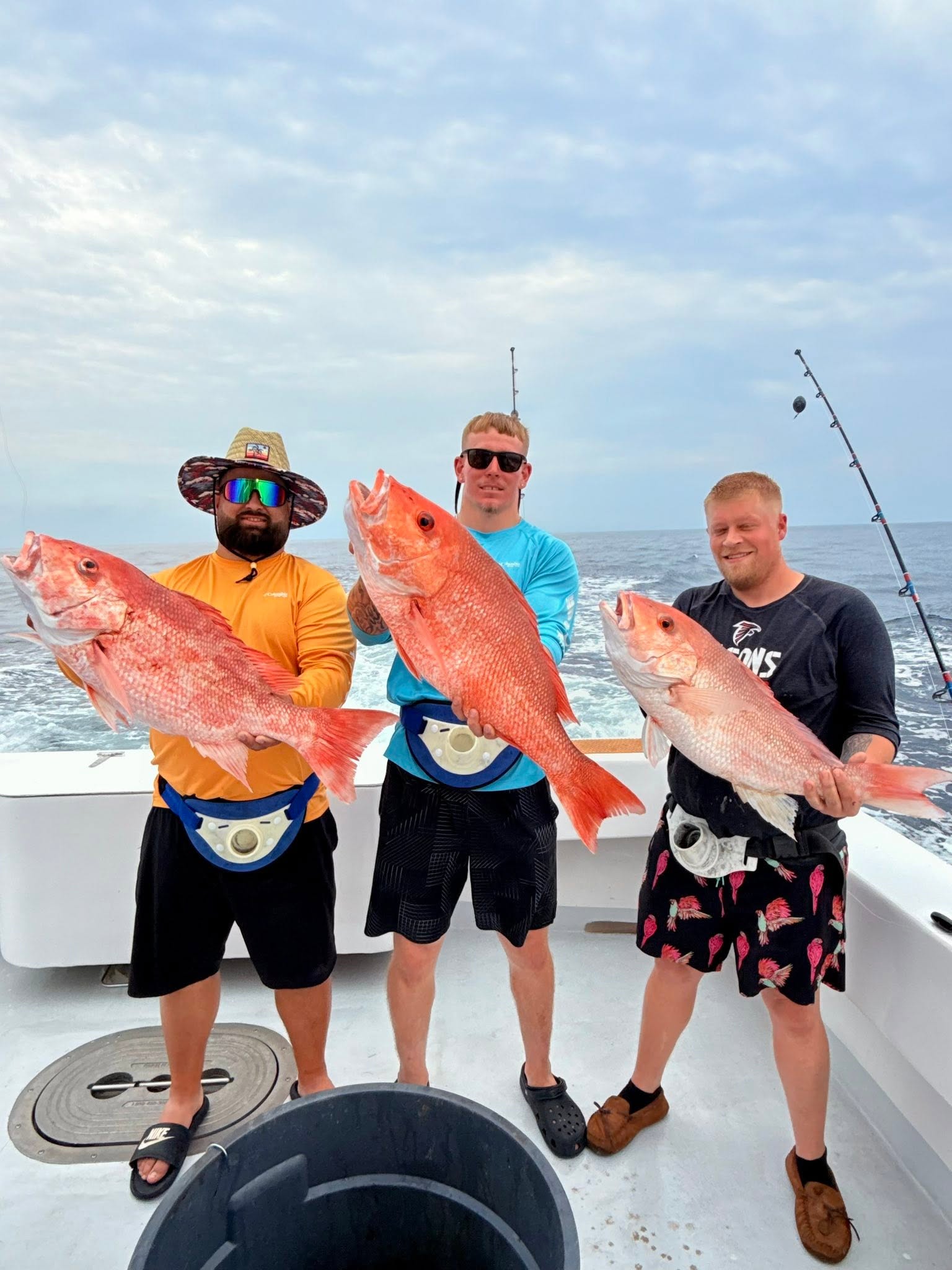 Three anglers on the stern of the Mighty Fine offshore, each holding a large red snapper