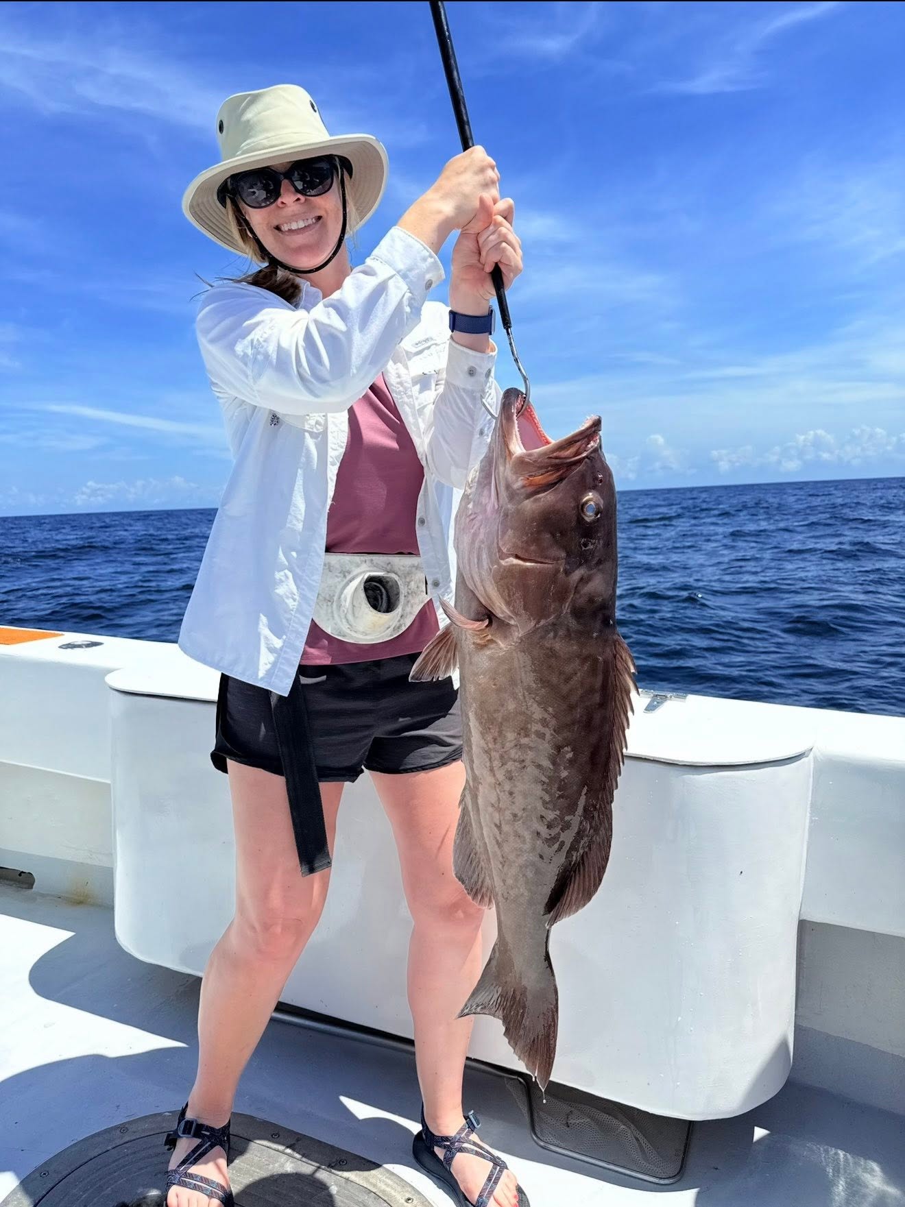 Smiling guest in a fighting belt holding a large gag grouper